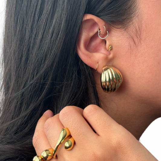 close up image of a model's ear showcasing gold filled jewelry including textured shell earrings and chunky gold statement rings