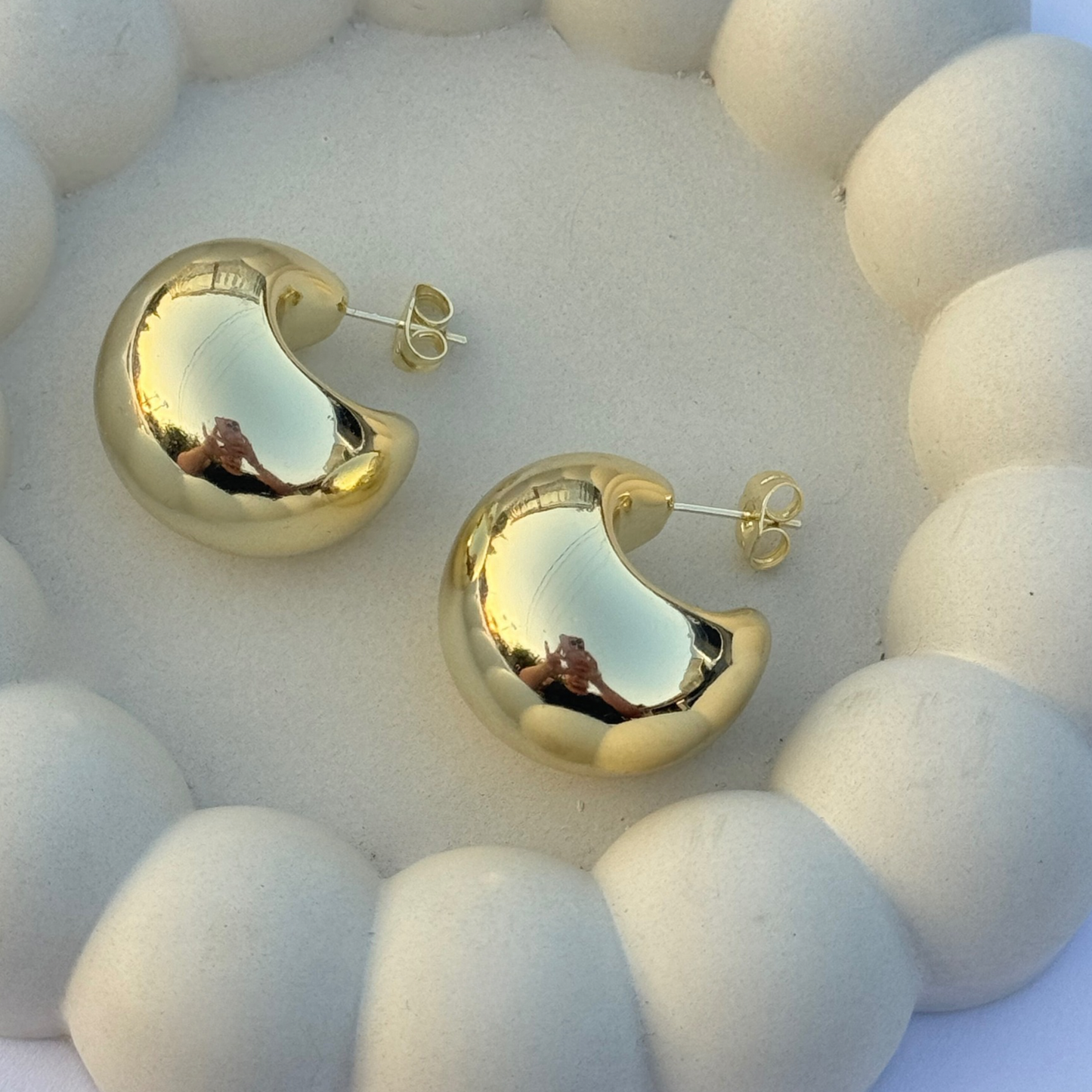 gold filled chunky crescent or moon shaped earrings displayed on a beige concrete jewelry dish