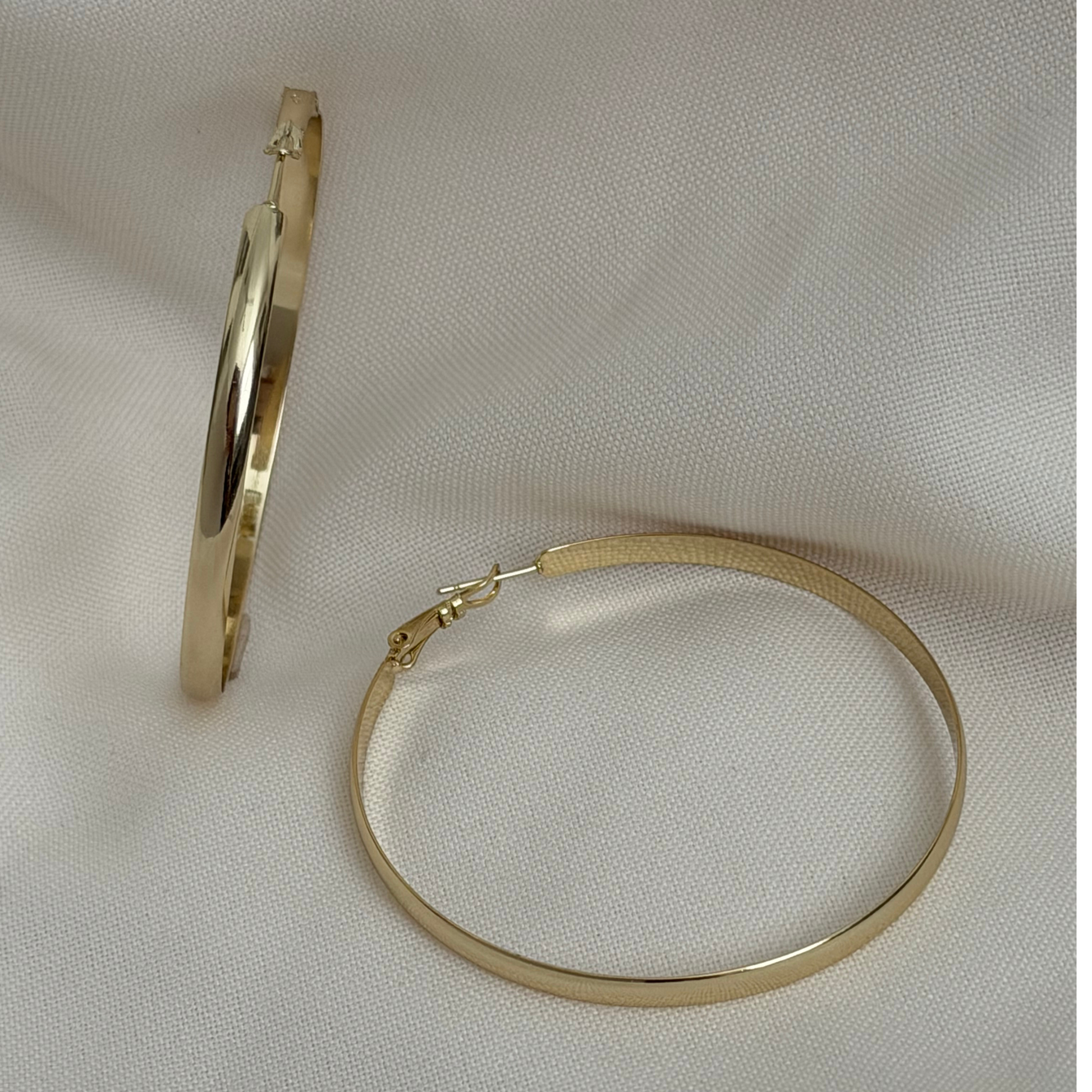 A pair of gold-toned hoop earrings displayed on a textured off-white fabric background..