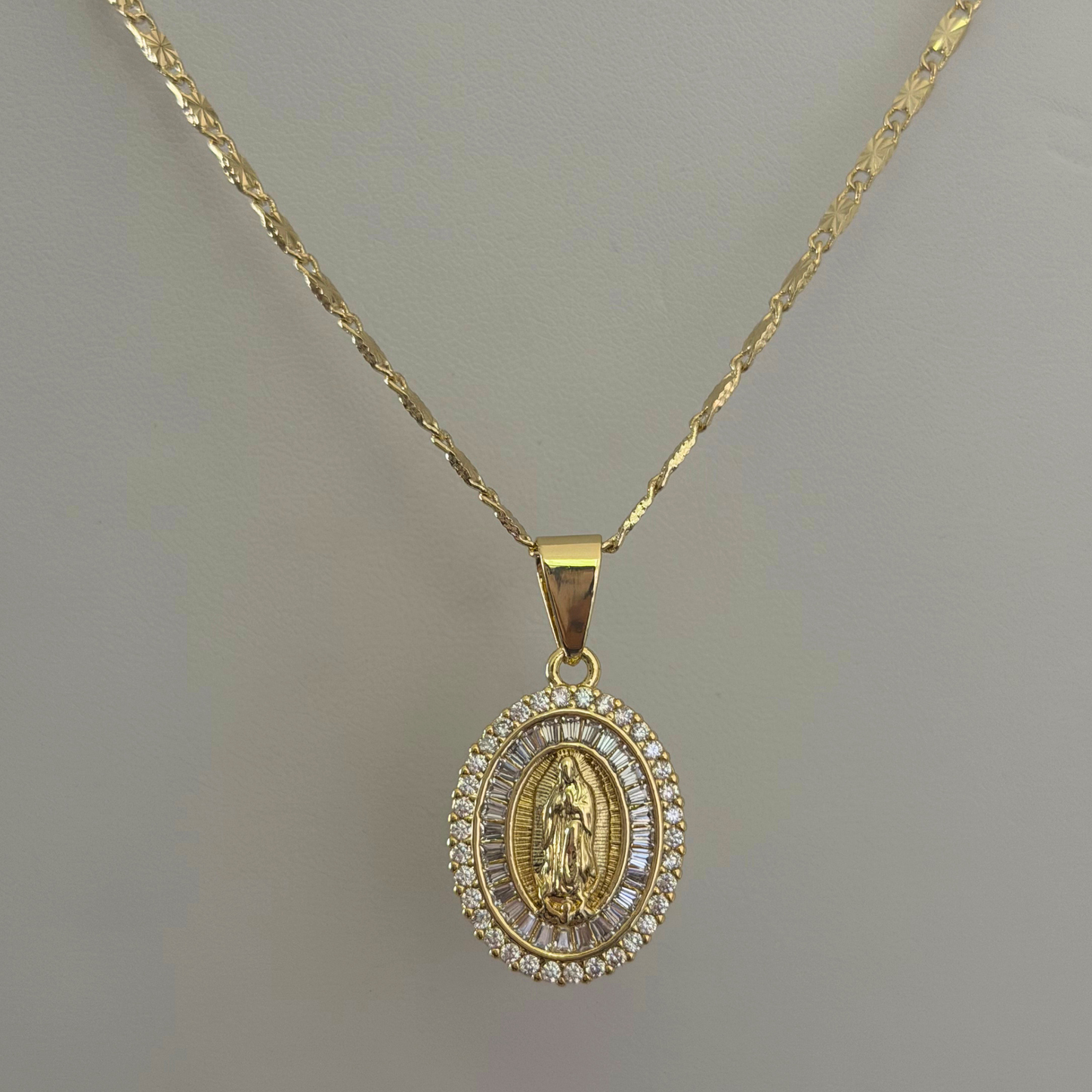 Close up image of Virgin Mary pendant of cubic zirconia stones hanging on a gold plated chain 