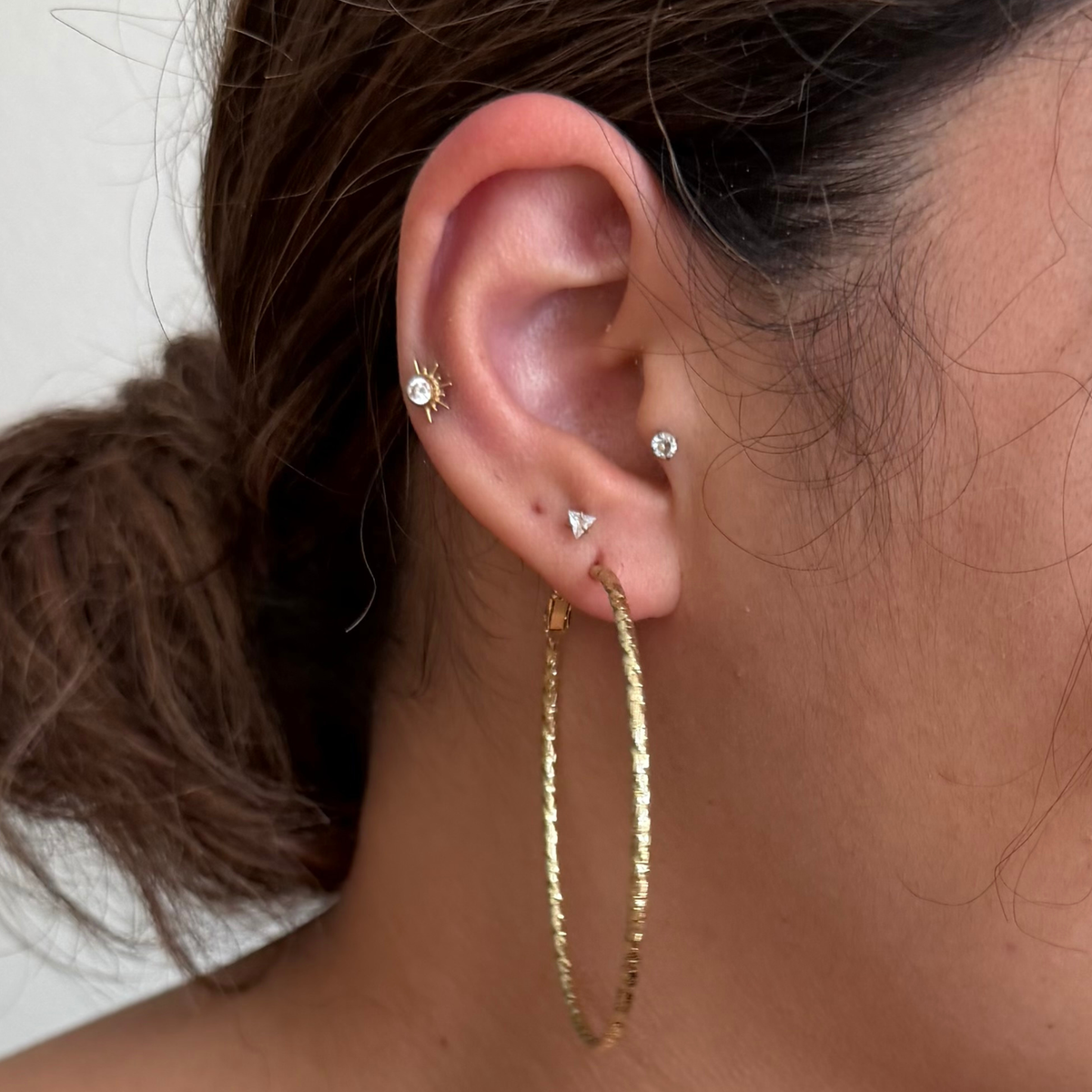 A close-up of a person's ear showcasing a pair of textured gold hoop earrings.
