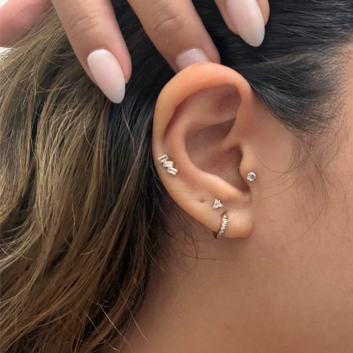 A close-up of a person's ear showcasing a stacked ear with various earrings including flat backs. 