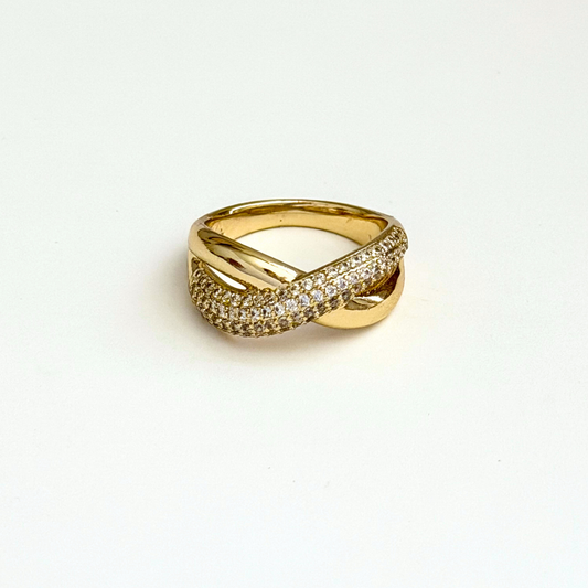 A gold ring with a twisted design, featuring one band paved with small cubic zirconia stones and the other with a polished gold finish, set against a plain white background.