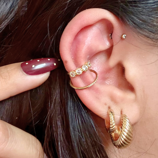 Close-up of an ear with gold hoop earrings and a ring, with a hand adjusting the jewelry.